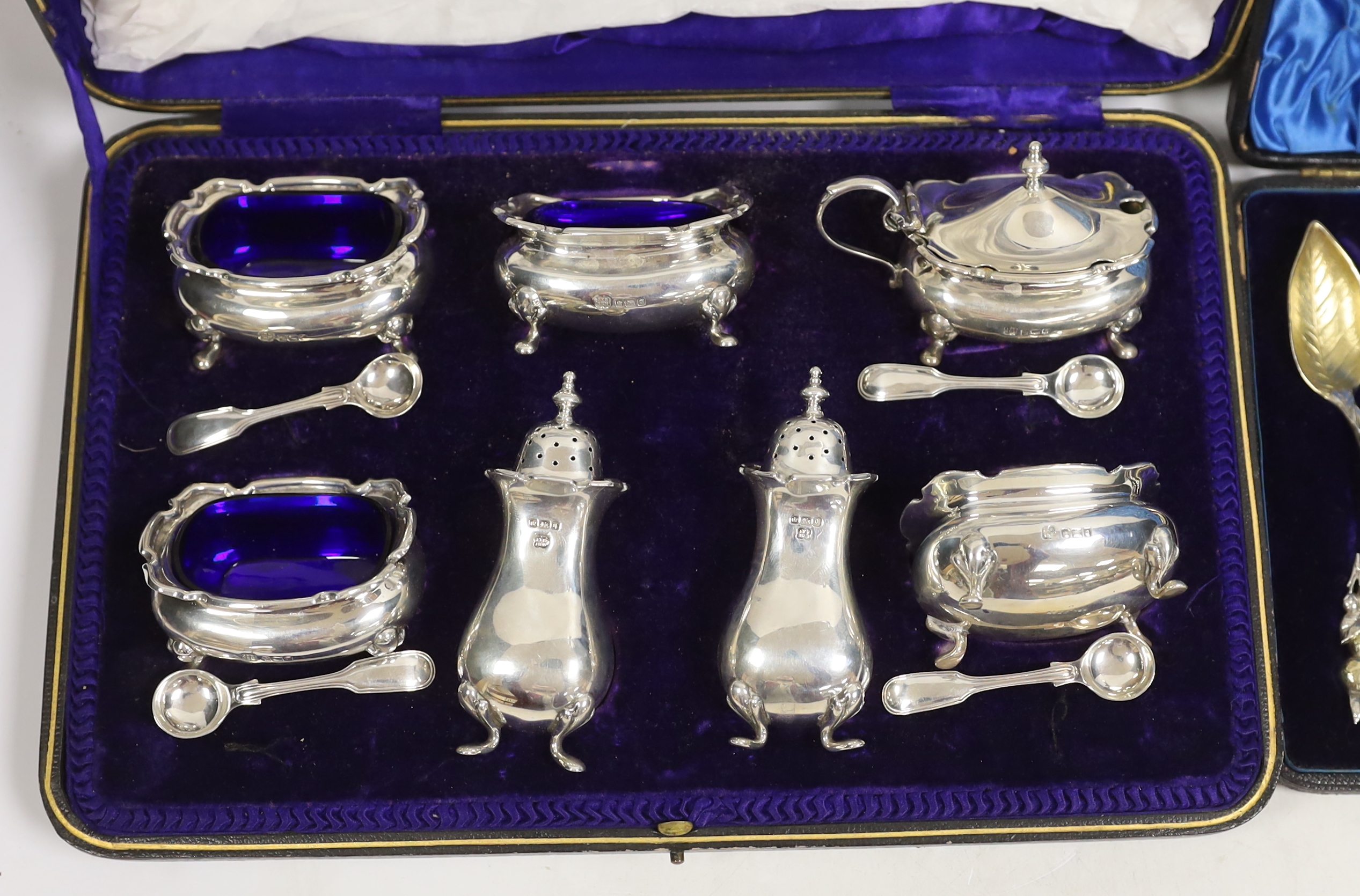 An Edwardian cased silver seven piece condiment set with four matching spoons, Hukin & Heath, Sheffield, 1908, together with an American cased set of parcel gilt sterling grapefruit spoons.